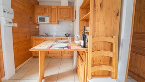 Une cuisine compacte dotée de meubles en bois, d’un four à micro-ondes et d’une table à manger pour deux personnes, avec des verres à vin et une bouteille.
