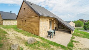 Un bâtiment en bois, de style grange, avec un toit en pente, des murs en pierre et une terrasse en gravier aménagée avec des sièges d’extérieur.