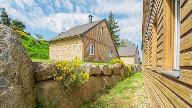 Une maison en pierre avec un toit en pente, un revêtement extérieur en bois et un mur de pierre à l’avant.