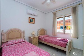A bedroom with two beds, a nightstand, an air conditioning unit, a window with curtains, and a picture on the wall. - CH Villa Sola Ciudad Quesada (Ciudad Quesada)