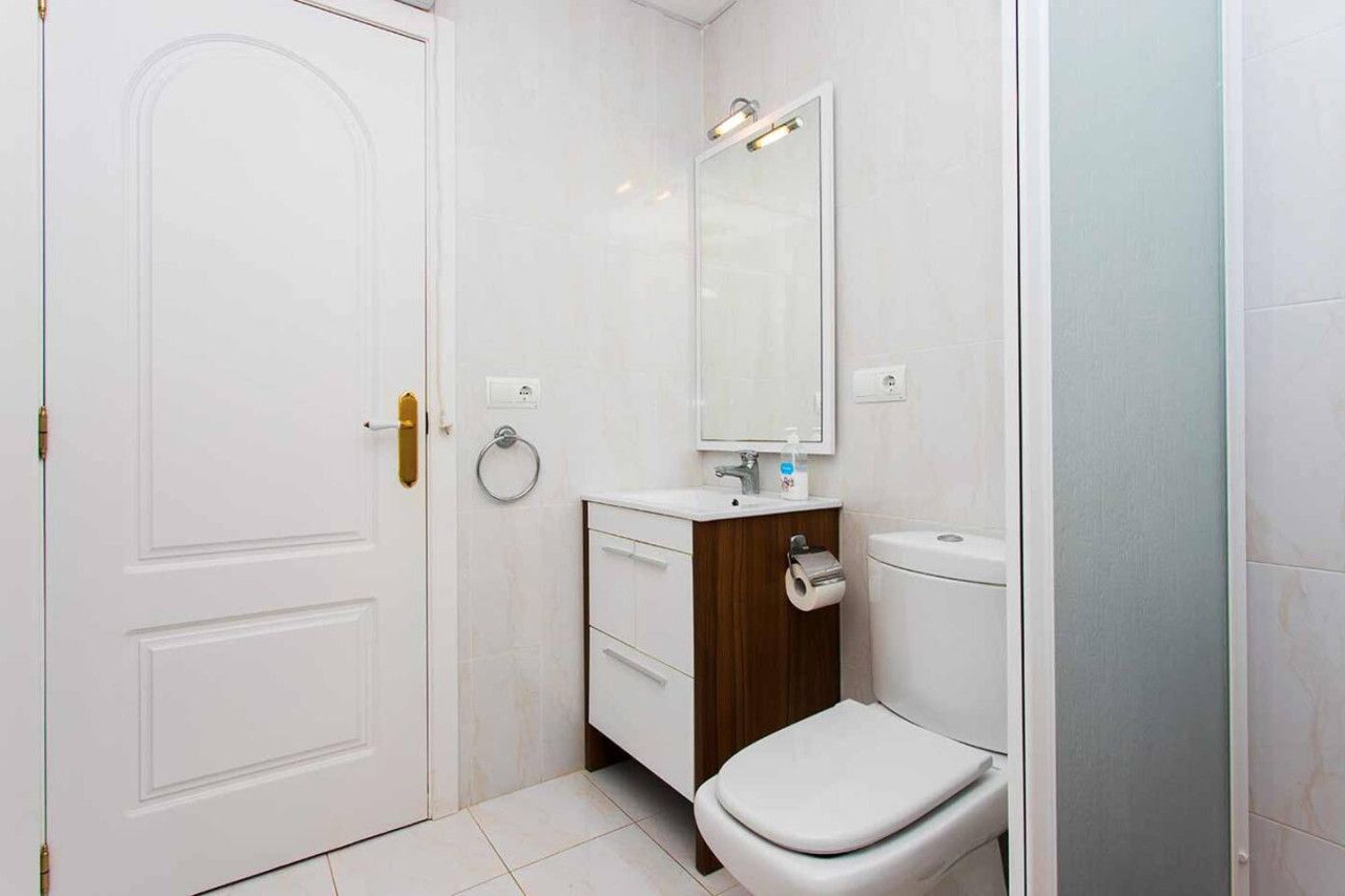 Un baño con una puerta blanca, un tocador de madera, un inodoro y un espejo.