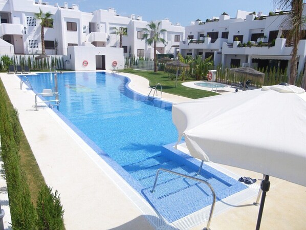 A swimming pool with a white poolside area, surrounded by modern white buildings with balconies.