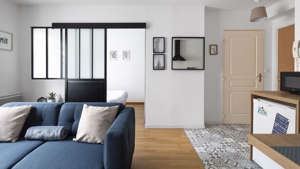Ein modernes Wohnzimmer mit einem blauen Sofa, einem kleinen Beistelltisch, einem Fernseher und einem Schrank.