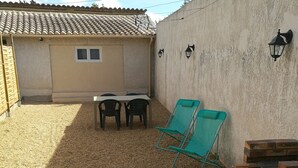 A patio with a table and chairs, a barbecue grill, and two lounge chairs.