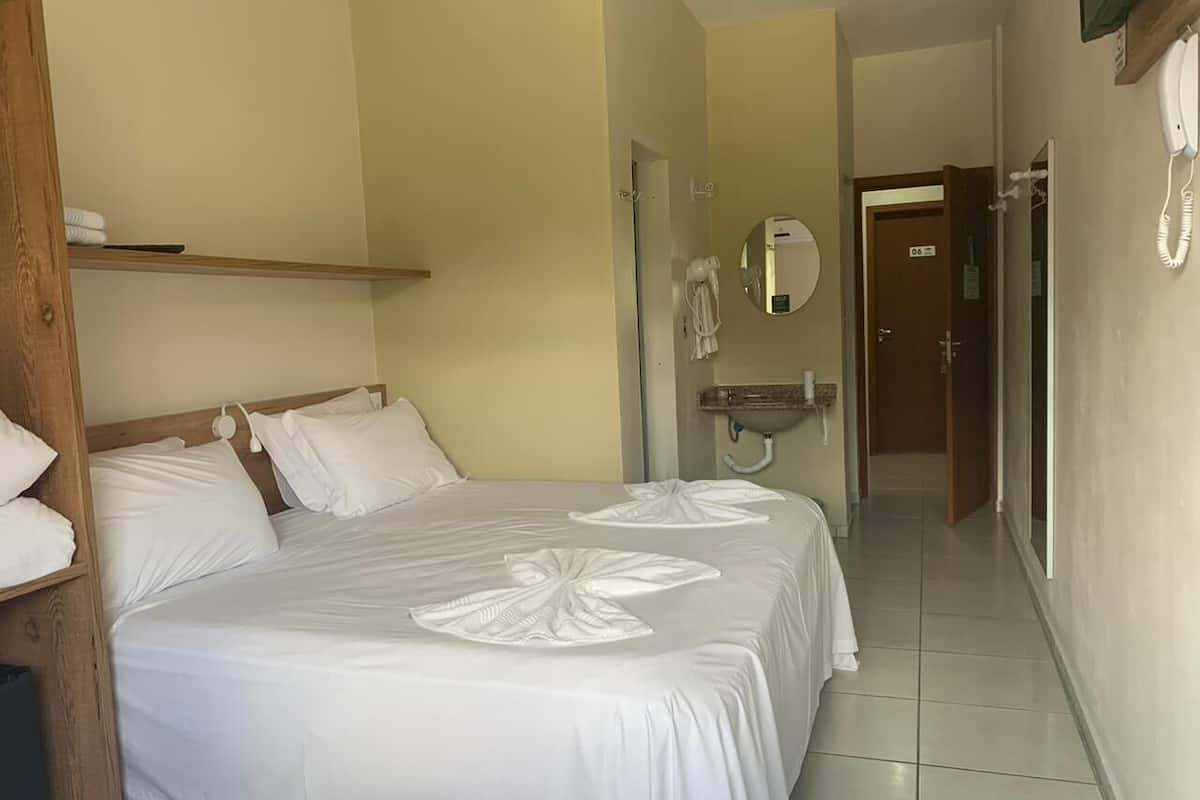 Ein Hotelzimmer mit einem großen Bett, einem Nachttisch, einem Spiegel und einem Telefon.