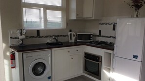 A compact kitchen with a washing machine, microwave, oven, and a refrigerator. - Hill Rise Retreat One (Harrow Park)