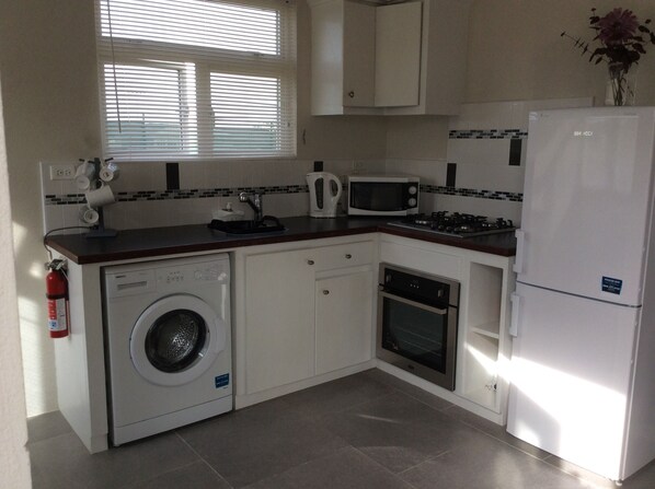 A compact kitchen with a washing machine, microwave, oven, and a refrigerator.