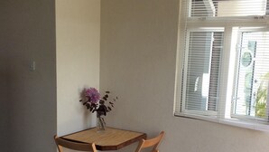 A small room with a wooden table and two chairs, a vase with flowers, and a window with blinds. - Hill Rise Retreat One (Harrow Park)