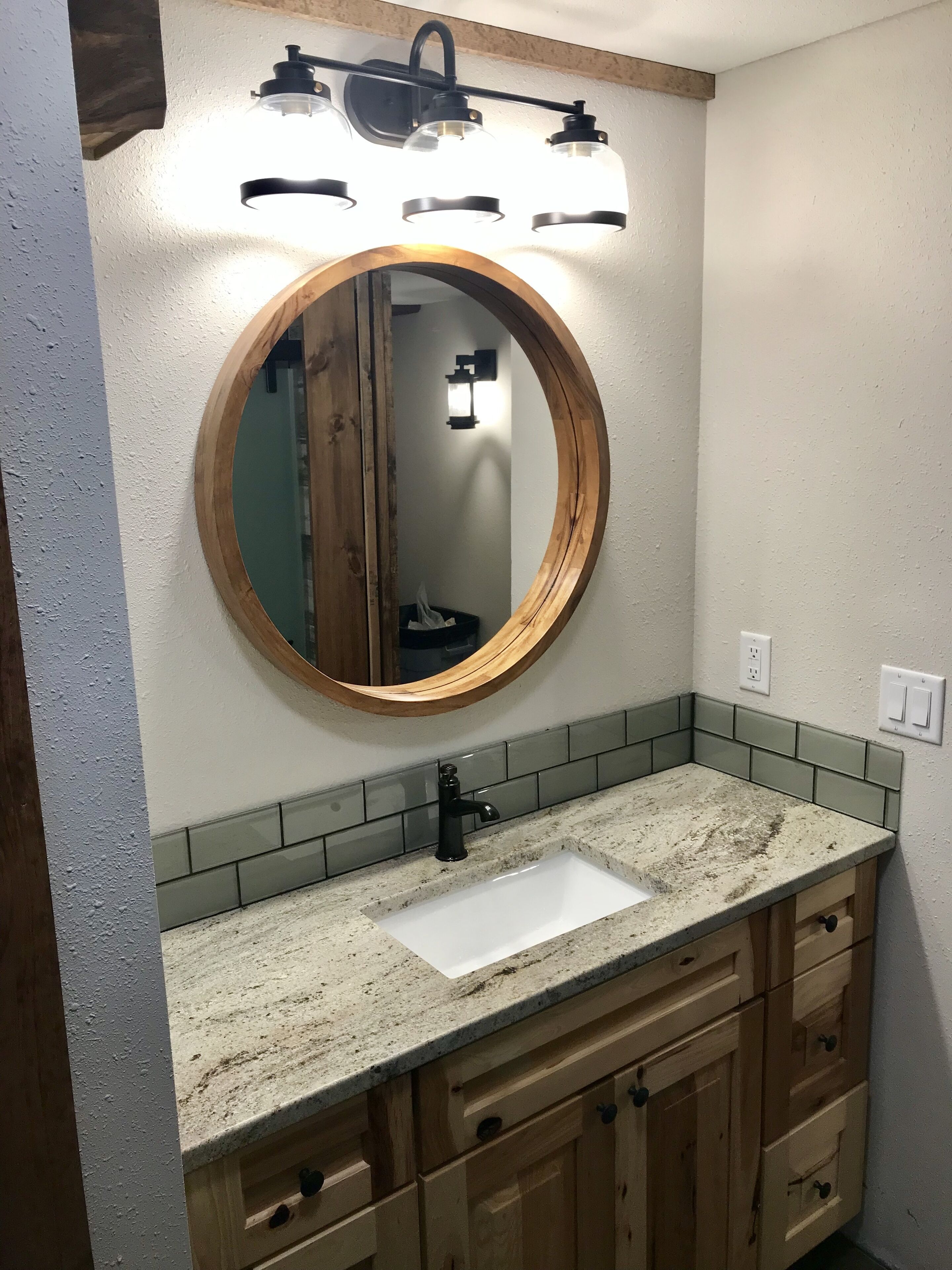 A bathroom with a wooden vanity, a round mirror, and a light fixture above the mirror.