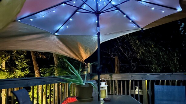 Uma área de estar ao ar livre com mesa, cadeiras e um grande guarda-sol com luzes de fada.