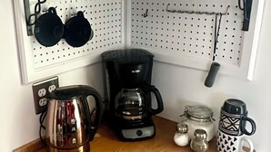 Uma cozinha compacta com micro-ondas, máquina de café, chaleira e canecas penduradas.