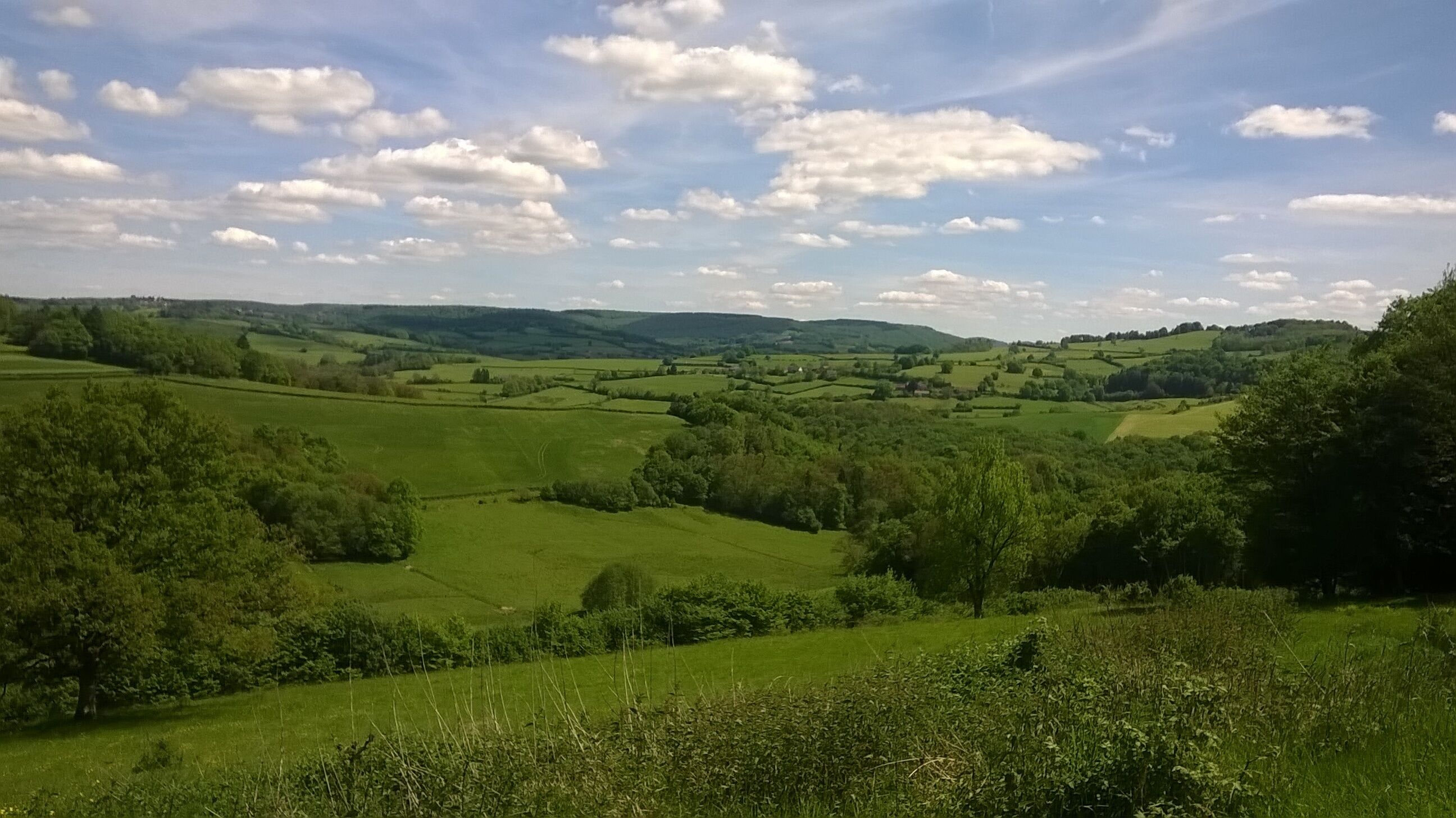 Een panoramisch uitzicht op glooiende groene heuvels en een heldere lucht met losse wolken.