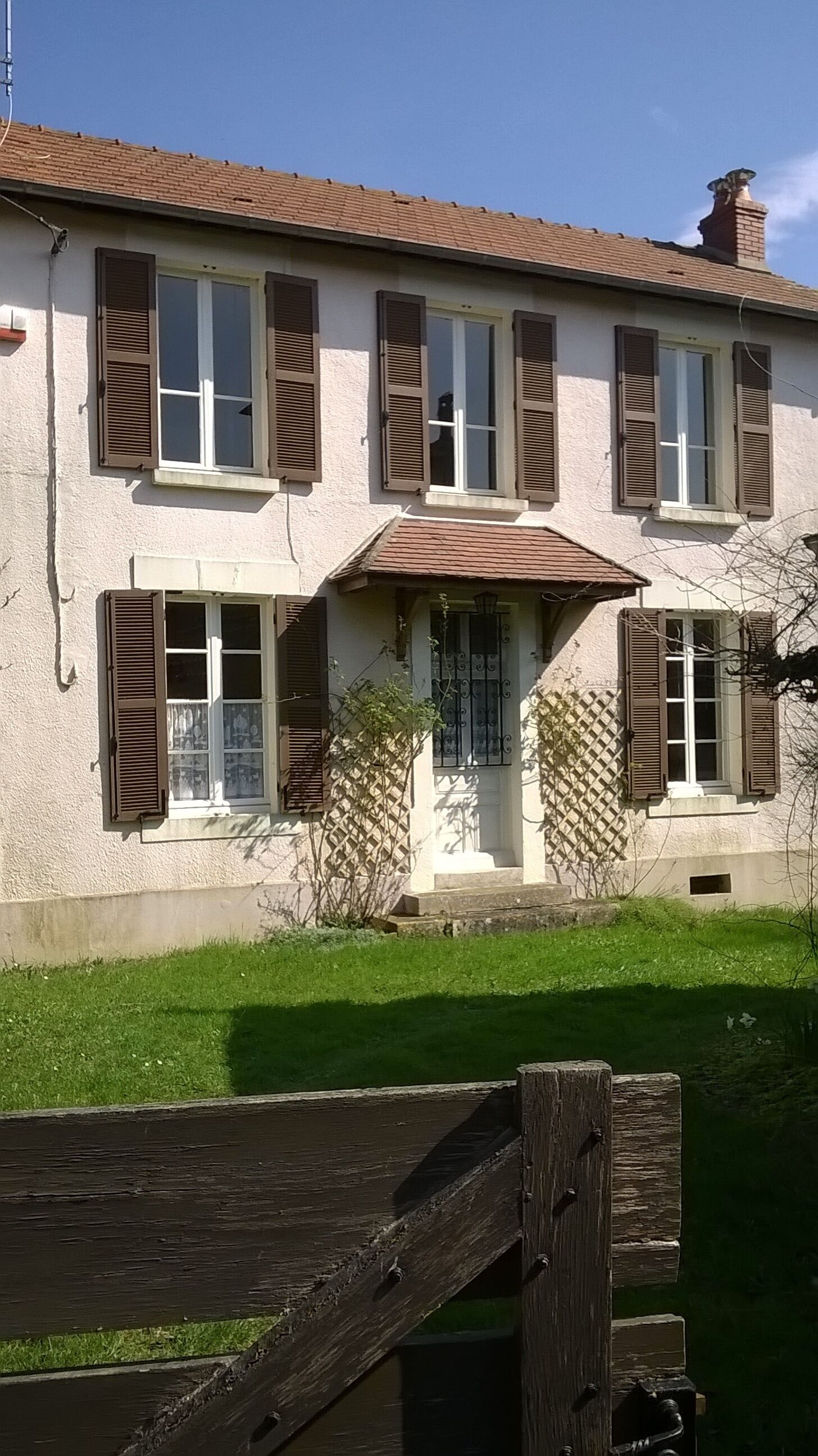 Un bâtiment à deux étages, doté d’un toit en tuiles, de nombreuses fenêtres avec volets et d’un petit porche à l’avant, agrémenté d’un portail en métal.