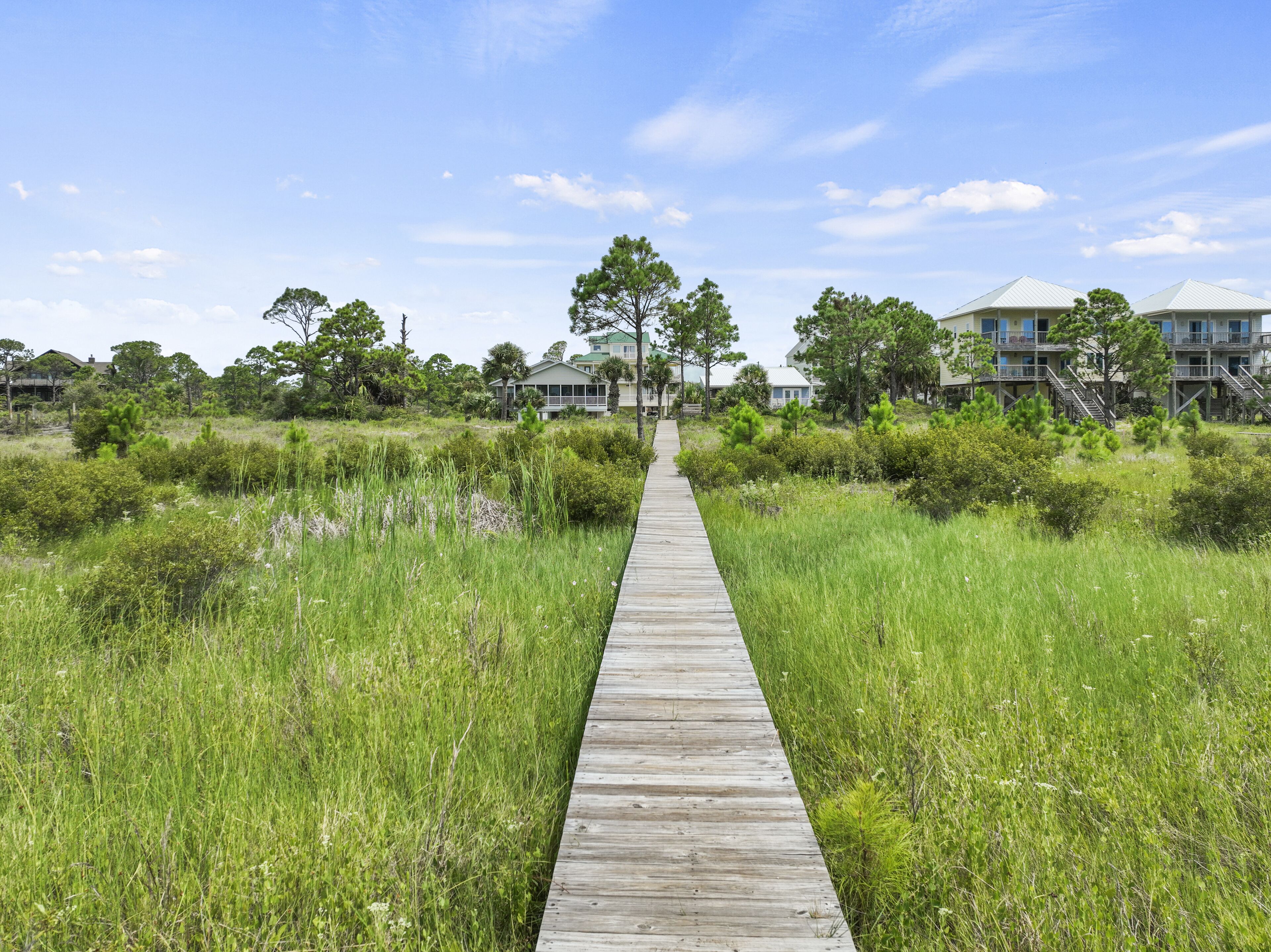 Une promenade en bois mène à une rangée de maisons situées en bord de mer, dotées de plusieurs étages et de balcons.