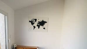 Huoneessa on puinen lipasto, valkoinen pöytä, jossa on kaksi tuolia, seinällä maailmankartta ja suuri ikkuna.