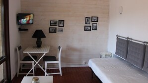 A small room with a bed, a TV, a table with chairs, and framed pictures on the wall. - Between CALVI and ILE ROUSSE  (Lumio)
