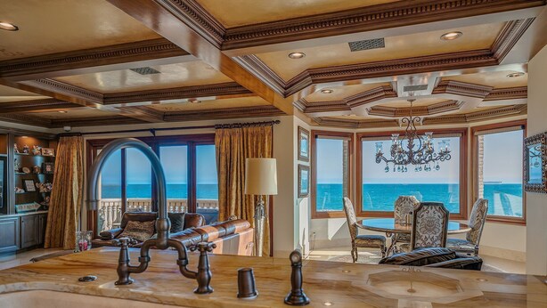 A luxurious room with a large wooden dining table, ornate ceiling, and a view of the sea. - Beach Front Executive Home (Long Beach)