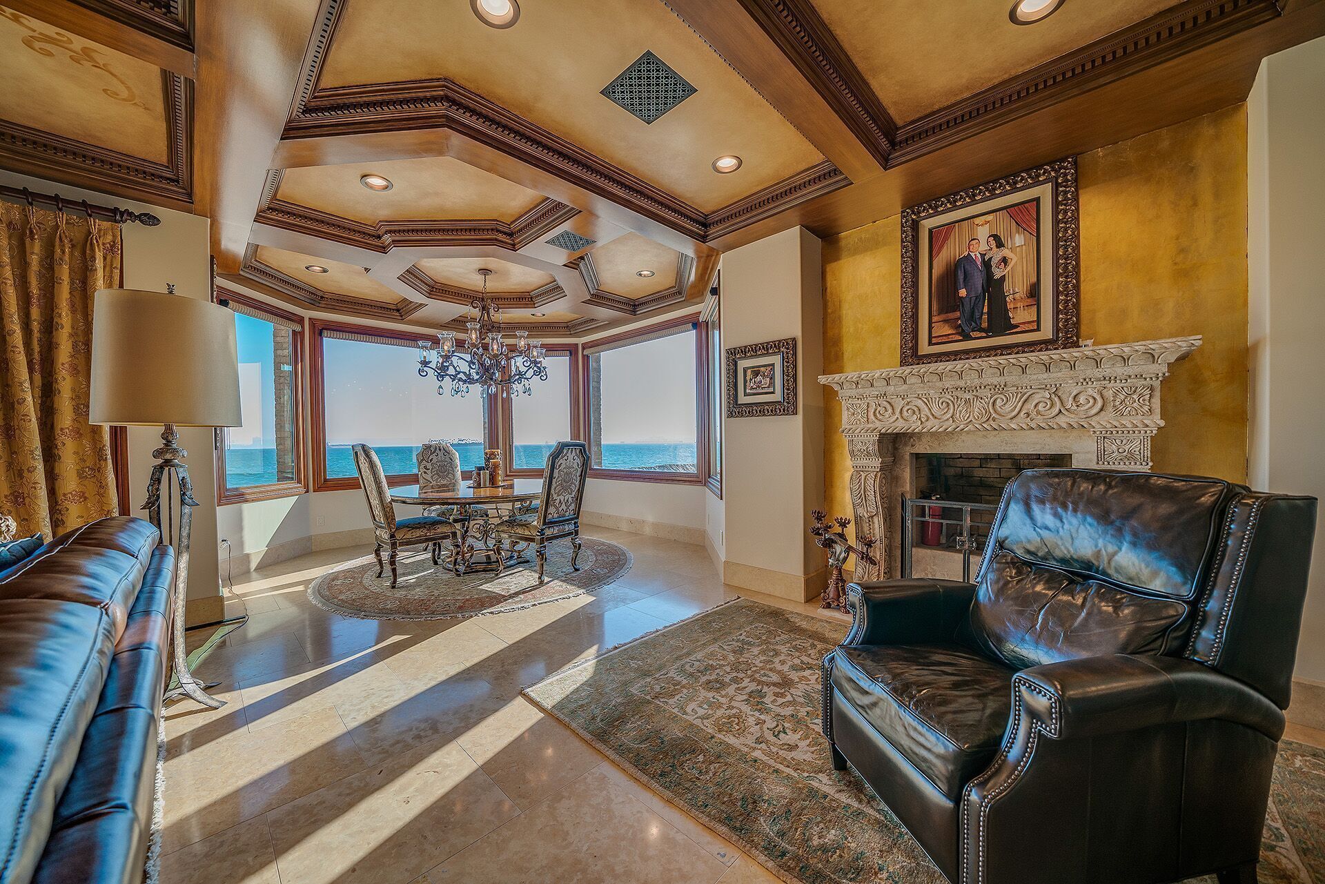 A spacious living room with a large window overlooking the sea, a fireplace, and a chandelier.