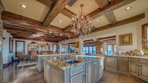 A spacious kitchen with a large island, wooden beams on the ceiling, and a view to the outside. - Beach Front Executive Home (Long Beach)