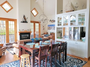 Amplia sala de estar con chimenea, muebles de madera, zona de comedor y cocina con armarios blancos y refrigerador de acero inoxidable.