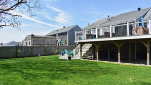 A residential backyard with a wooden deck, a covered patio, and a fenced area. - Three bedroom home- quick stroll to Nantucket Sound Beaches (Dennis Port)