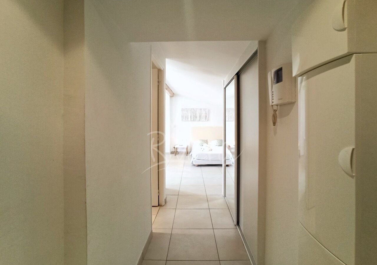 A hallway leading to a bedroom with a bed, a bedside table, and a nightstand.