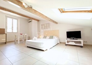 A bedroom with a bed, a desk, a chair, a TV on a stand, and a skylight.