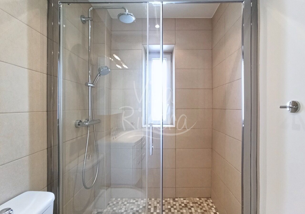 A glass-enclosed shower with a handheld showerhead and a wall-mounted faucet.