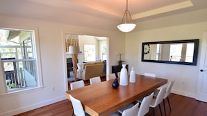 A dining area with a wooden table and white chairs, a hanging light fixture, and a large mirror on the wall.