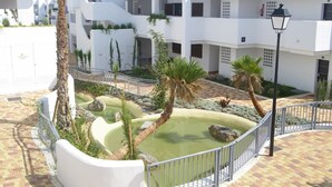 A courtyard with a water feature, palm trees, and white buildings with balconies. - Apartamento Platano (Mar de Pulpi) (San Juan de los terreros)
