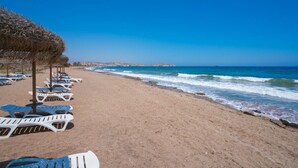 A beach with rows of white lounge chairs and thatched umbrellas. - Apartamento Platano (Mar de Pulpi) (San Juan de los terreros)