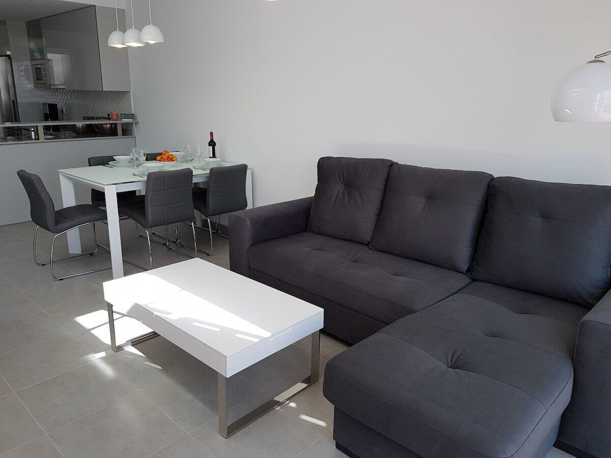 En moderne stue med en grå sofa, et hvidt sofabord og et spiseområde med et hvidt bord og stole.