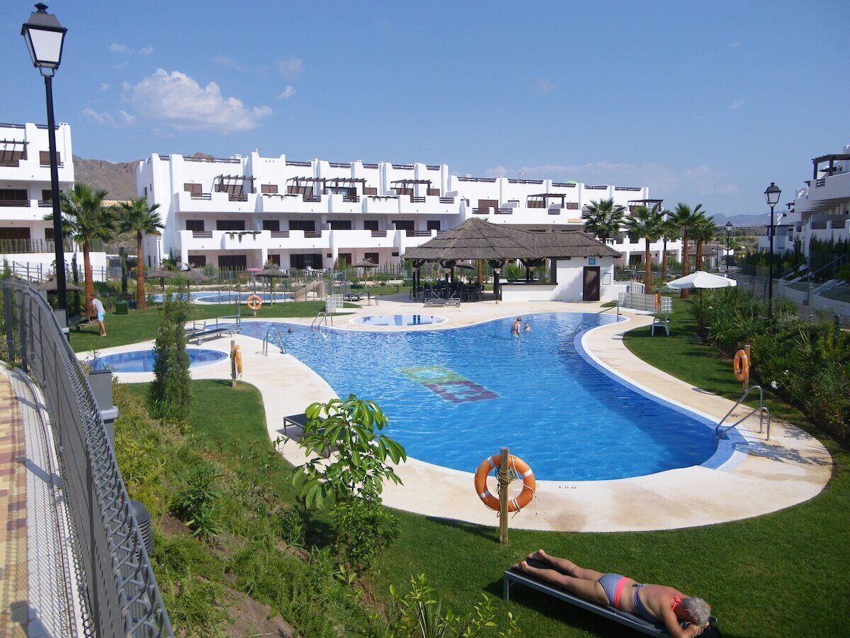 Una piscina de borde curvo, rodeada de césped y palmeras.
