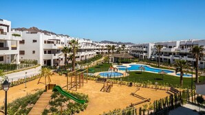 A resort with multiple white buildings, a central pool area with a slide, and a clear view of the surrounding landscape. - Apartamento Platano (Mar de Pulpi) (San Juan de los terreros)