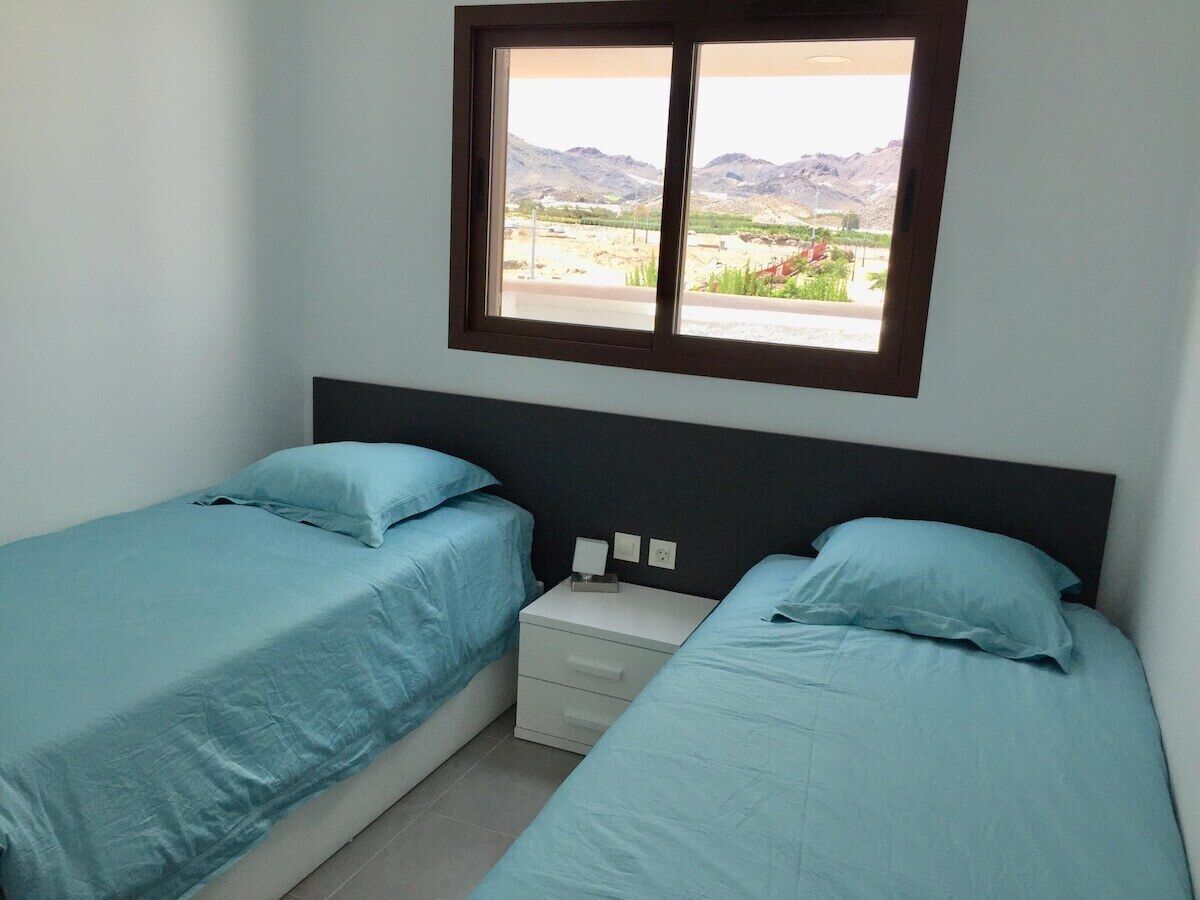 Una habitación con dos camas, una mesita de noche y una ventana con vistas a un paisaje montañoso.