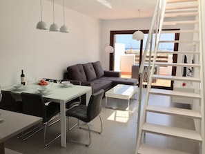 Ein modernes Wohnzimmer mit Essbereich, einer Couch, einem Couchtisch und einer Treppe, die zu einem Außenbalkon führt.