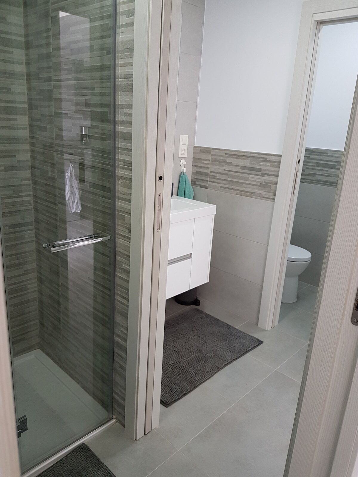 Un baño moderno con cabina de ducha de vidrio, un lavabo blanco y un inodoro.