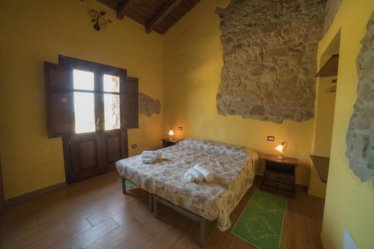 A bedroom with a wooden bed, a stone wall, a wooden door, and two bedside lamps.