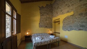 Un dormitorio con cama, suelo de madera, pared de piedra y una ventana.
