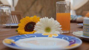 Una mesa con un plato, un vaso de zumo de naranja y dos flores.