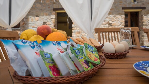 Una mesa con una cesta de frutas frescas, pan y alimentos envasados.