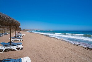 A beach with rows of sun loungers and a thatched umbrella.