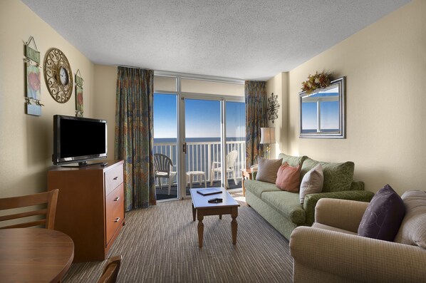 Une chambre d’hôtel avec un balcon, une télévision, un canapé et une table à manger.