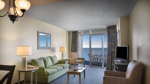 A hotel room with a green sofa, a striped armchair, a small table, a TV, and a balcony with curtains. - Oceanfront 2 Bedroom Condo w/ Amazing View + Official On-Site Rental Privileges (Myrtle Beach)