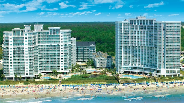 A beachfront hotel complex with multiple high-rise buildings, a pool area, and a beach with umbrellas. - Oceanfront 2 Bedroom Condo w/ Amazing View + Official On-Site Rental Privileges (Myrtle Beach)