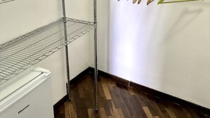 Un armario con estantes metálicos, suelo de madera y pared blanca con un mueble pequeño.