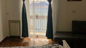 Un dormitorio con cama, ventana con cortinas, radiador y un cuadro en la pared.
