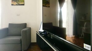 Una sala de estar con un televisor de pantalla plana grande, un sofá gris y un cuadro de un paisaje costero en la pared.