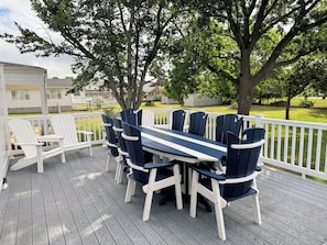 A deck with a table and chairs, surrounded by white railings and trees.