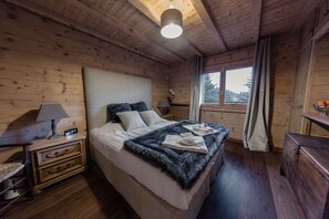 Un dormitorio de cabaña de madera con cama, mesitas de noche, lámpara y ventana con cortinas.